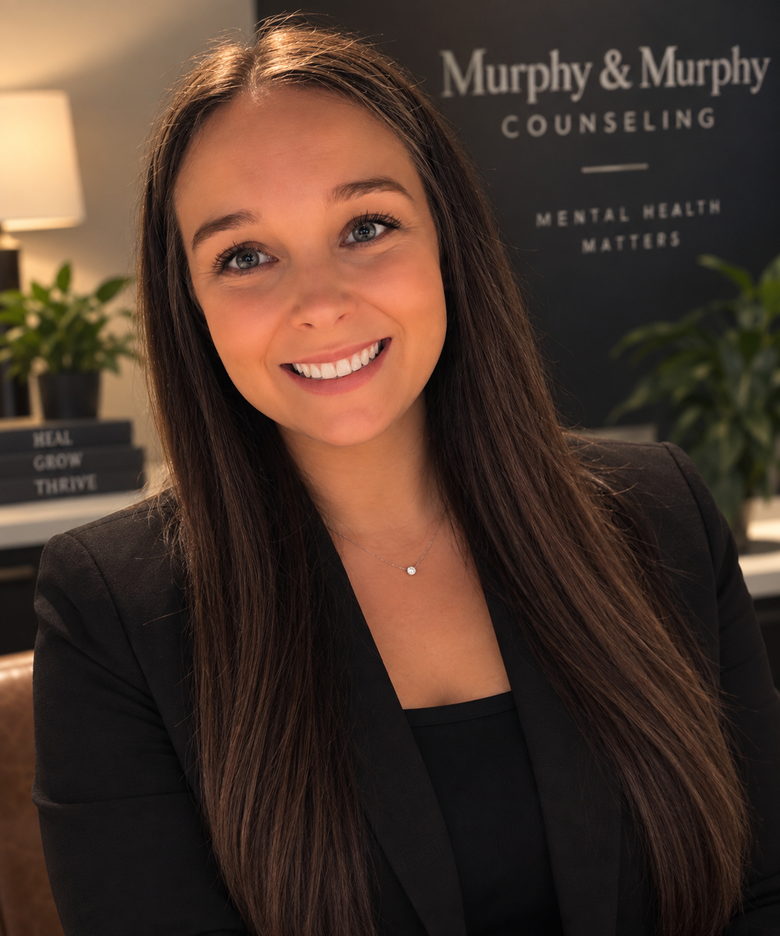 Tiffany Murphy, in a black jacket, in front of the Murphy and Murphy Counseling sign in the practice&rsquo;s office.